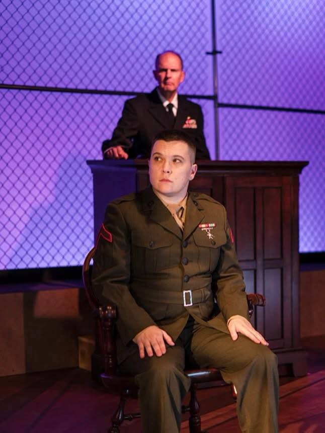 A seated Marine and another uniformed performer appear at a courtroom podium.