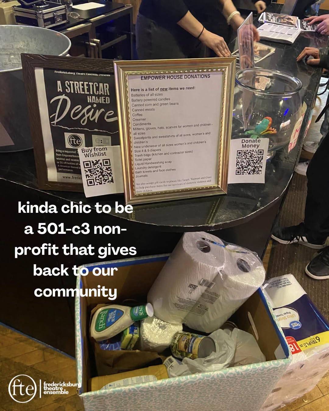 A lobby table of collected Empower House donations beside an A Streetcar Named Desire poster, over the words “kinda chic to be a 501-c3 non-profit that gives back to our community”.