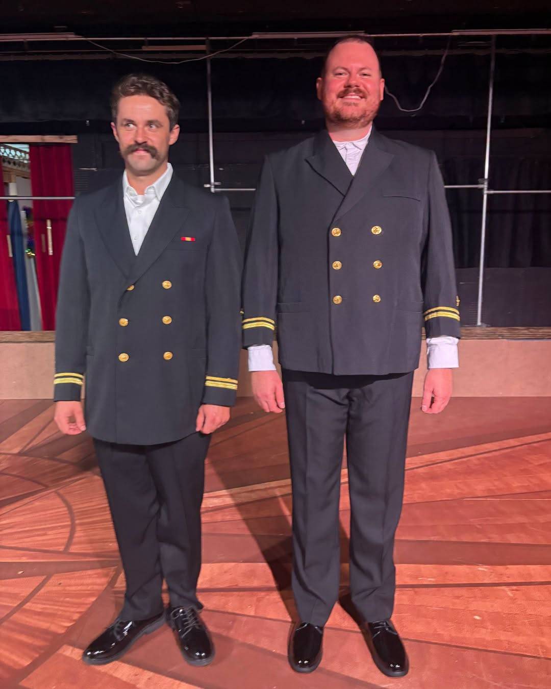 Two performers stand side by side on stage in Navy service dress jackets with gold buttons and sleeve stripes.